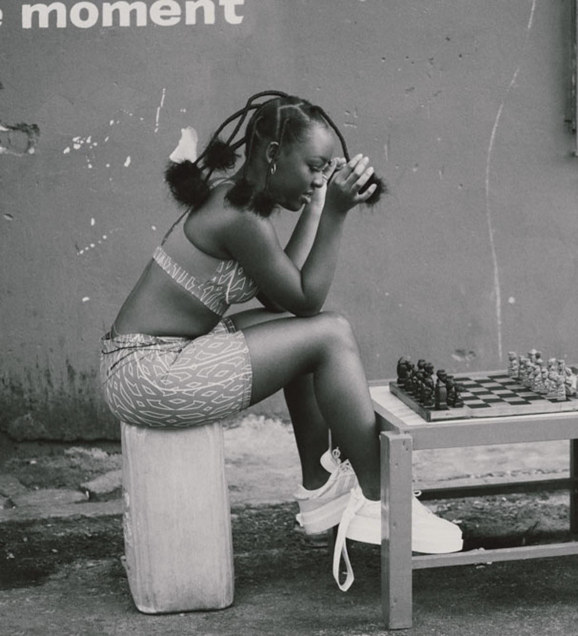Elsa Majimbo assise devant un échiquier en extérieur, portrait en noir et blanc