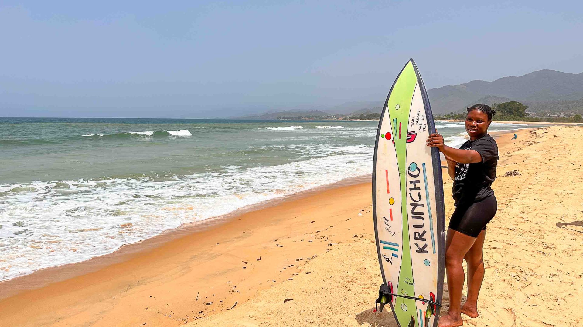 Kadiatu Kamara debout sur la plage, tenant sa planche de surf