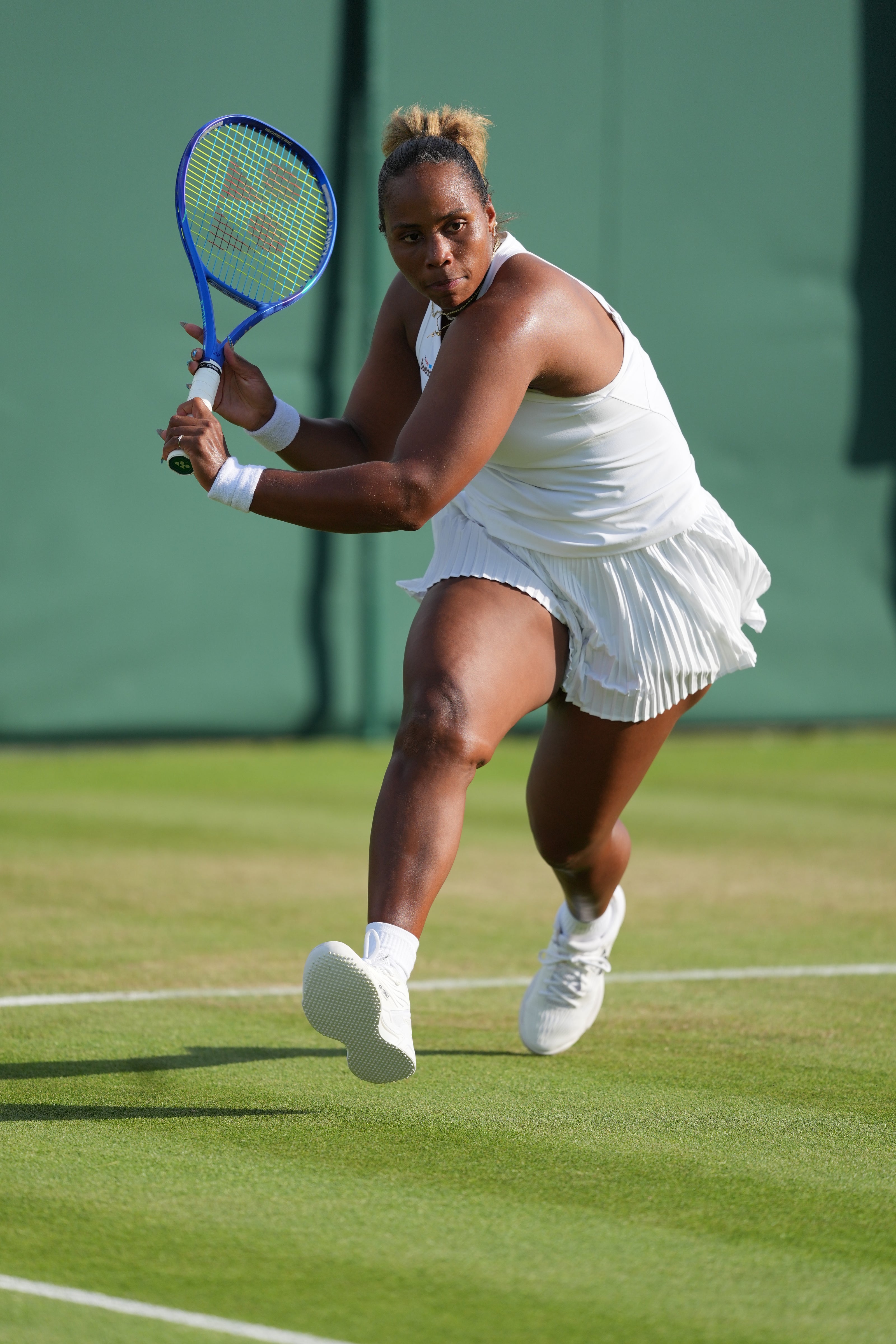 Taylor Townsend, en tenue blanche, tient une raquette bleue devant une paroi verte