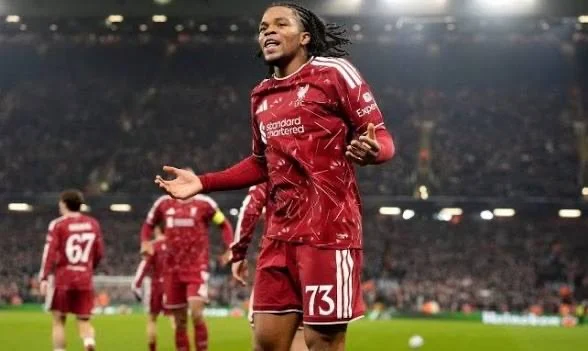 Un joueur de Liverpool en tenue rouge célèbre sur la pelouse, les bras écartés.