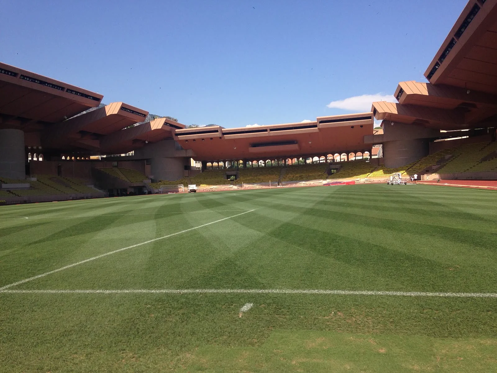 The pitch and stands of the Stade Louis-II in Monaco under a blue sky.