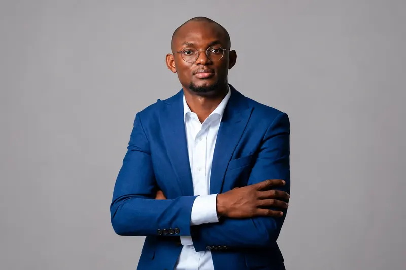 Mamady Doumbouya en costume bleu, les bras croisés. Portrait officiel Feguifoot retouché avec IA pour retirer l’habillage graphique.