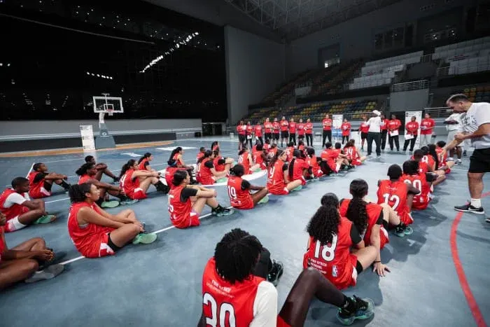 Young female players sitting on the court listen to a coach during a FIBA Africa camp