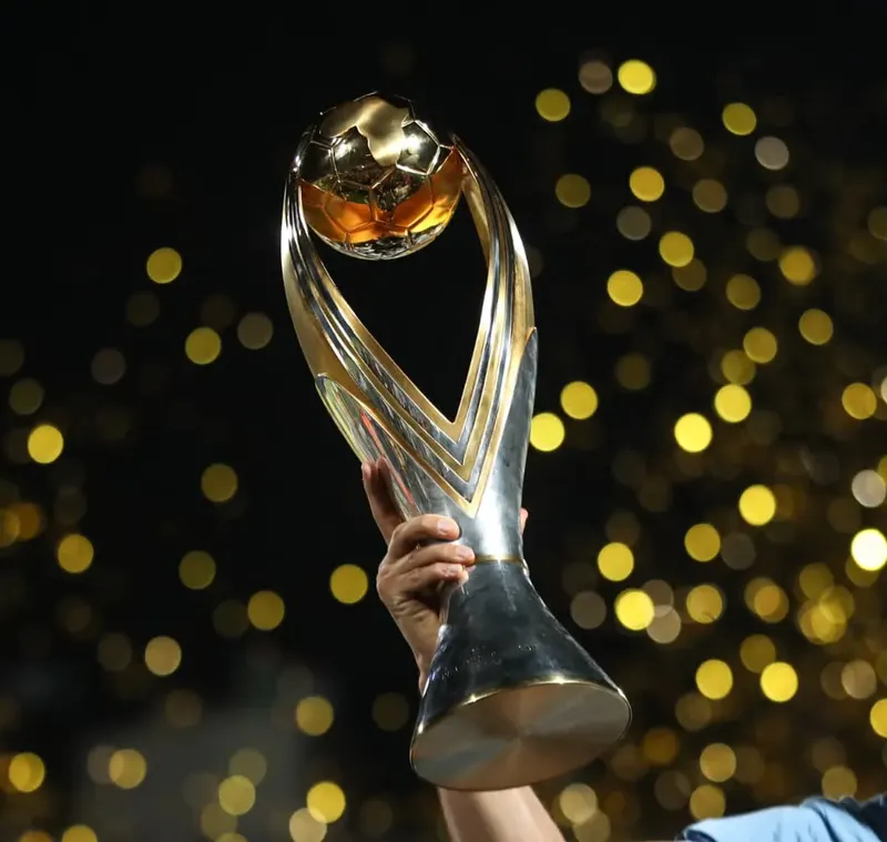 Illustration: the CAF Champions League trophy held aloft against a dark, golden background.