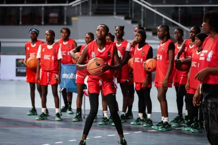 A young female player, ball in hand, in front of her team-mates at a FIBA Africa camp