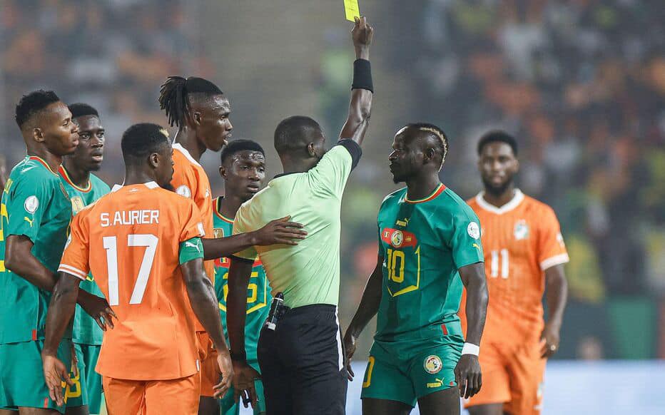 TOPSHOT - Gabonese referee Pierre Atcho (C) shows a yellow card to Senegal's midfielder #10 Sadio Mane (2R) during the Africa Cup of Nations (CAN) 2024 round of 16 football match between Senegal and Ivory Coast at the Stade Charles Konan Banny in Yamoussoukro on January 29, 2024. (Photo by KENZO TRIBOUILLARD / AFP)