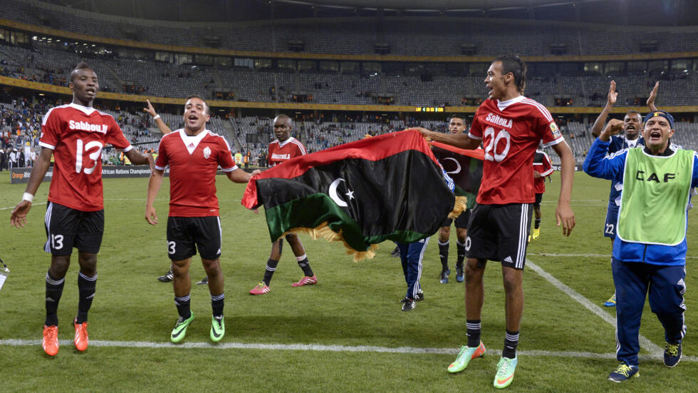 Libya team players hold their national flag as they celebrate after winning the African Nations Championship football final match between Ghana and Libya, in Cape Town, on February 1, 2014.  AFP PHOTO / ALEXANDER JOE